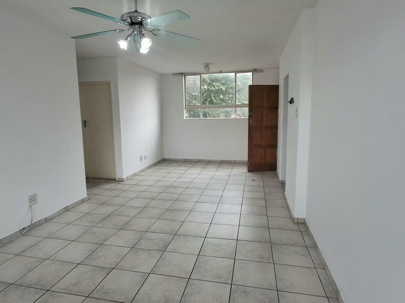 An empty, open-plan living area featuring neutral white walls, tiled flooring, and a ceiling fan, offering a blank canvas for interior design.