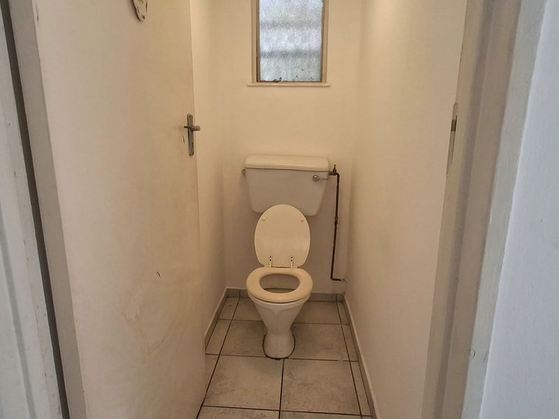 A compact, functional bathroom featuring a standard toilet, tiled flooring, and an obscured glass window for privacy.