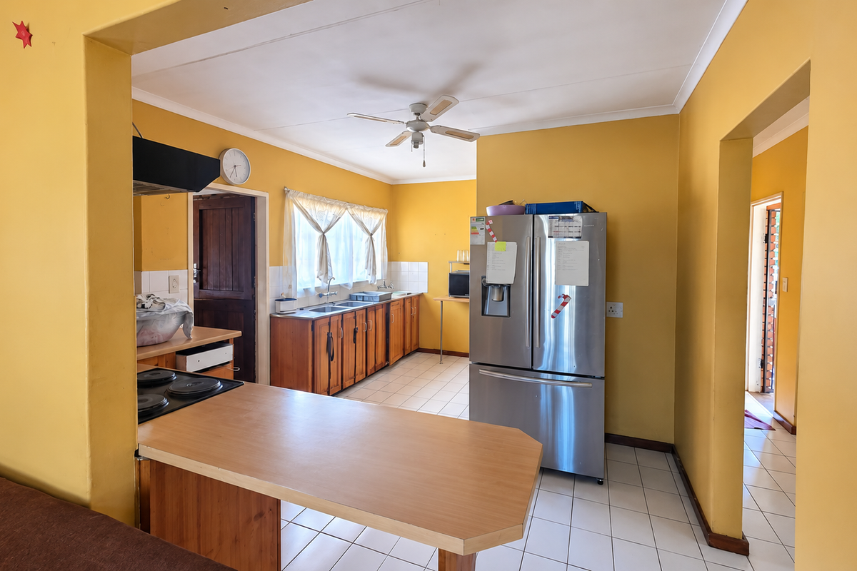 A functional kitchen featuring wooden cabinetry, a built-in hob with extractor, and tiled flooring, offering a practical layout with potential for modern updates.