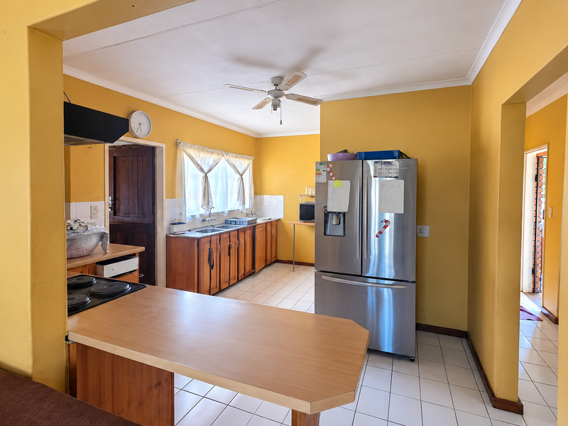 A functional kitchen featuring wooden cabinetry, a built-in hob with extractor, and tiled flooring, offering a practical layout with potential for modern updates.