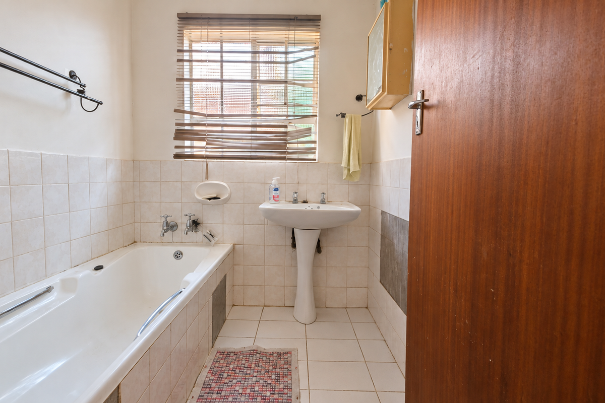 A functional bathroom featuring a pedestal basin, built-in bathtub, and tiled finishes, offering potential for modernization and cosmetic updates.