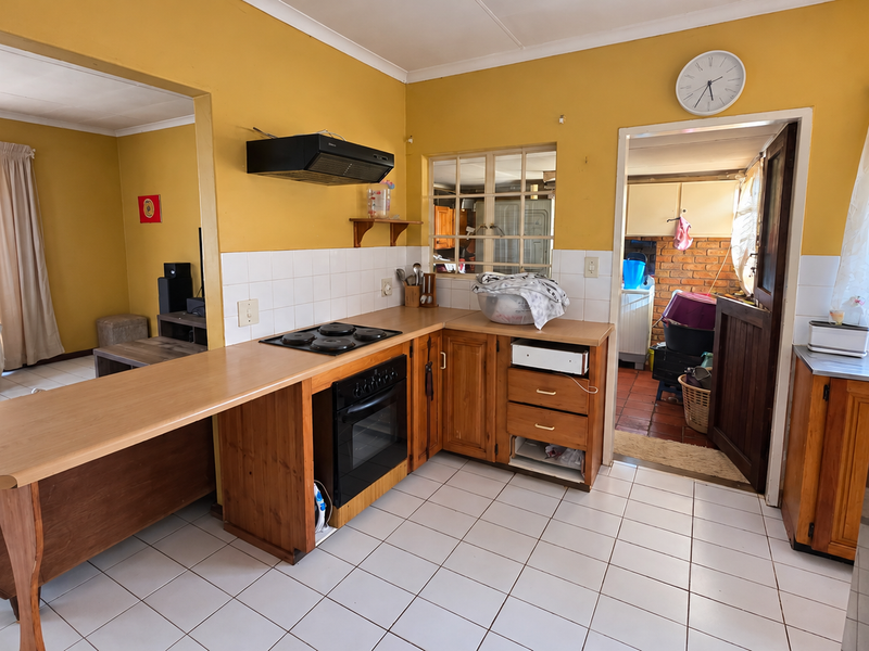 A functional kitchen featuring wooden cabinetry, laminate countertops, built-in oven and hob, and tiled flooring, with an open-plan layout connecting to the living area.