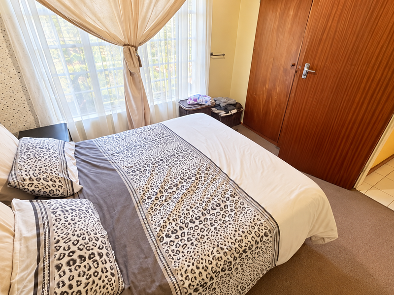 A functional bedroom featuring built-in wooden wardrobes, carpeted flooring, and a window with natural light, offering a comfortable and practical living space.