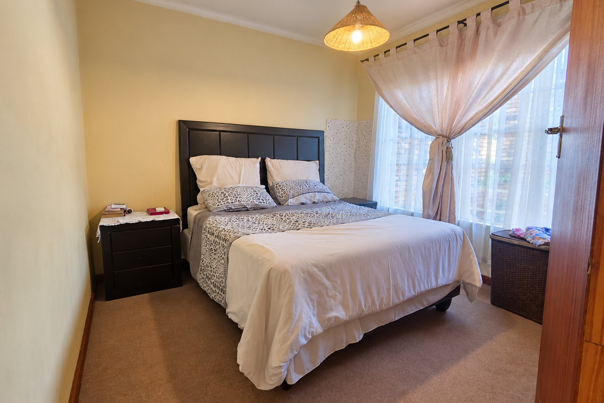 A cozy bedroom featuring carpeted flooring, a built-in headboard, and natural light through large windows with installed curtain tracks.