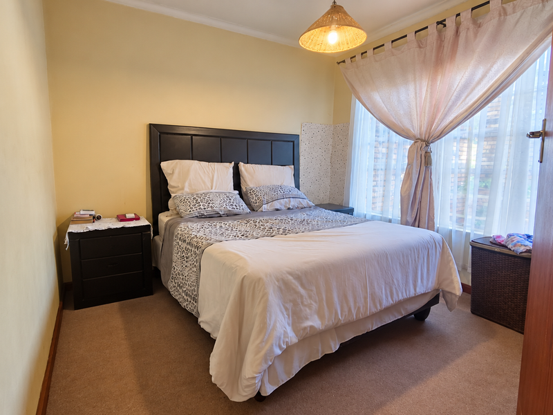 A cozy bedroom featuring carpeted flooring, a built-in headboard, and natural light through large windows with installed curtain tracks.
