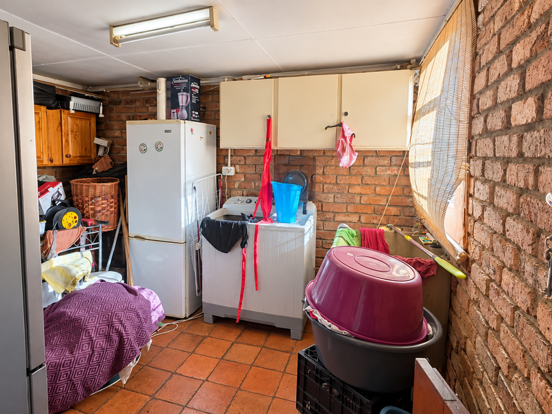 A functional laundry area featuring exposed brick walls, terracotta floor tiles, and built-in cabinetry, providing a practical space for utility and washing needs.
