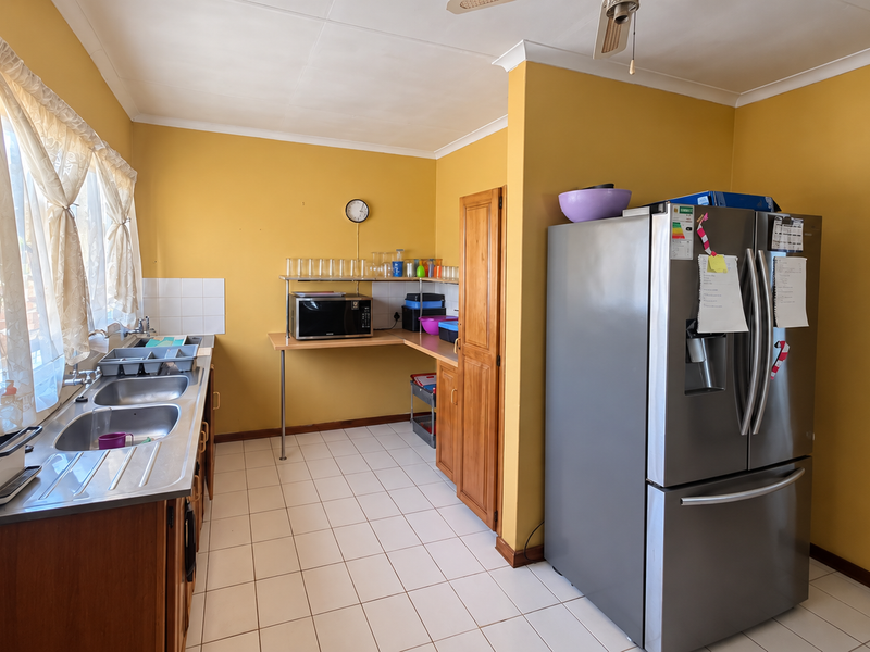 A functional kitchen featuring tiled flooring, a double stainless steel sink, built-in wooden cabinetry, and a tiled splashback.