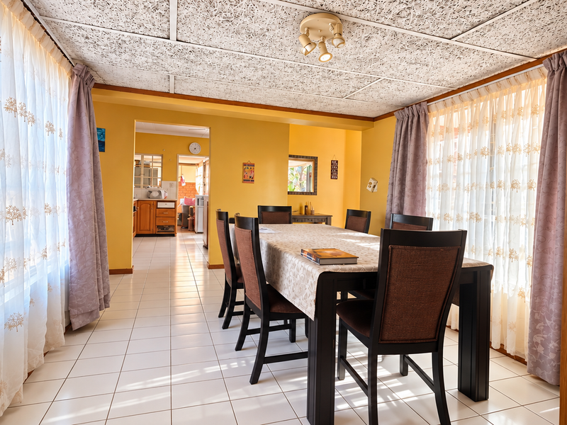 A dining room featuring tiled flooring and a textured ceiling, with an open-plan layout leading into the kitchen area.