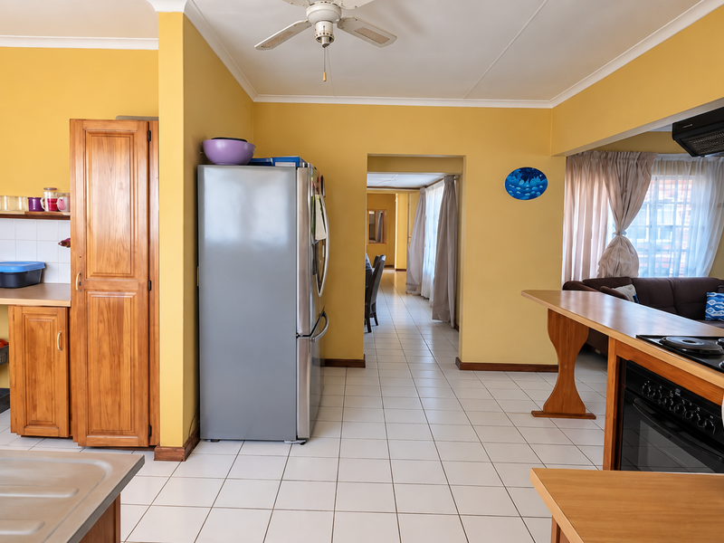 A functional kitchen featuring wooden cabinetry, tiled flooring, a built-in oven with hob, and an extractor fan, with an open-plan layout leading to the living area.