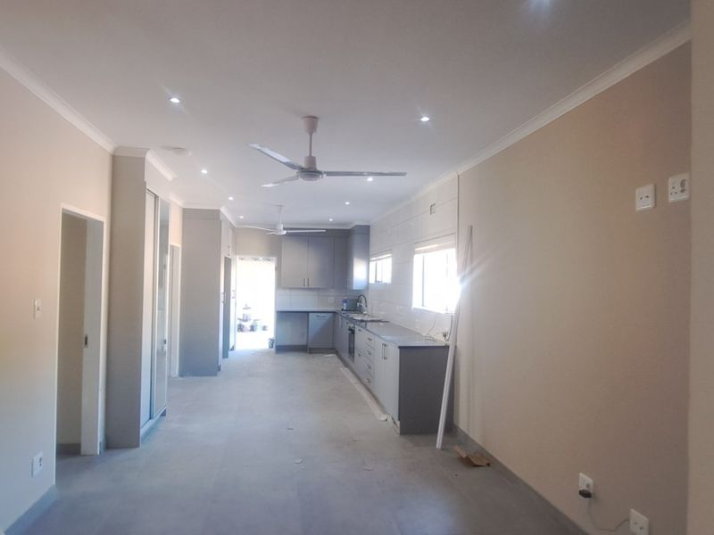 Spacious open-plan living and kitchen area featuring modern grey cabinetry, tiled floors, recessed lighting, and ceiling fans in a neutral, well-maintained setting.