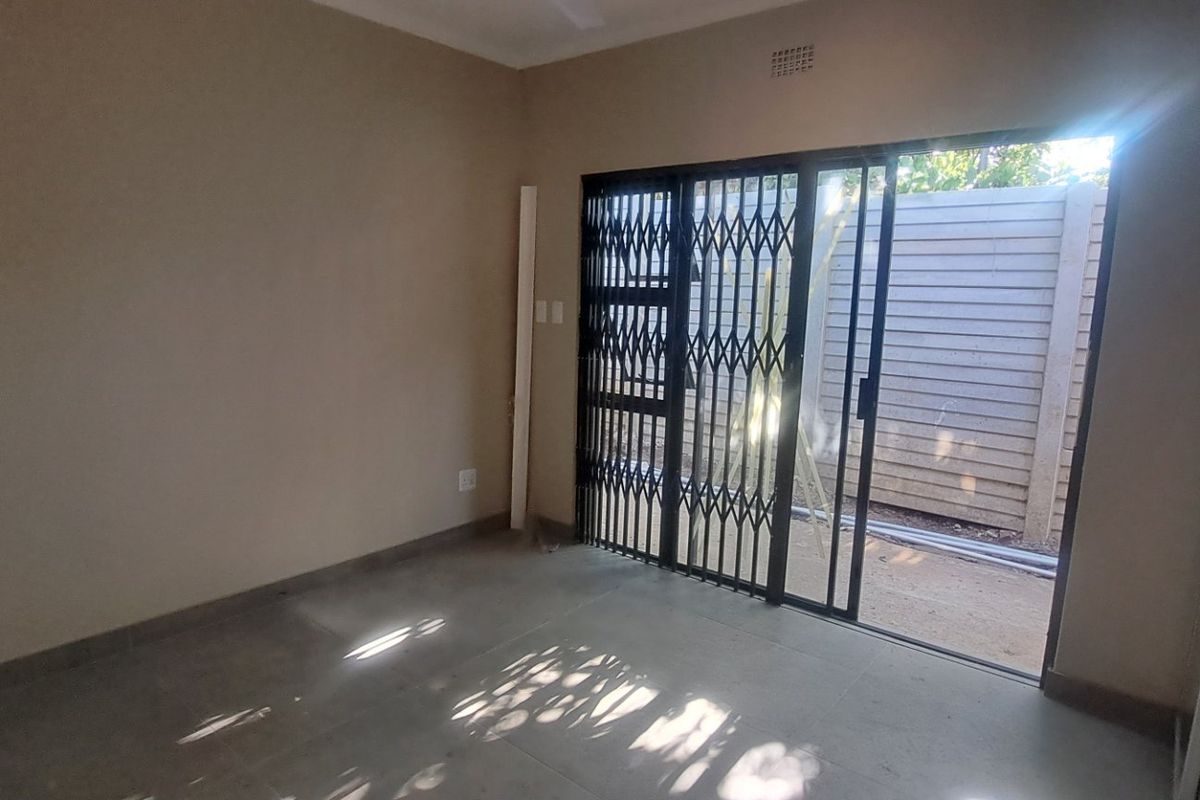 An empty living room featuring tiled flooring and a sliding glass door with a security gate leading to an outdoor area.