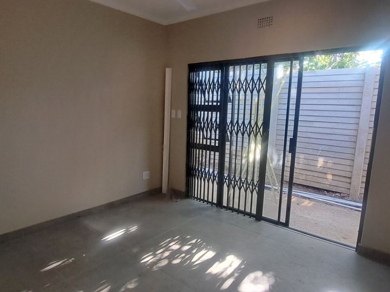 An empty living room featuring tiled flooring and a sliding glass door with a security gate leading to an outdoor area.