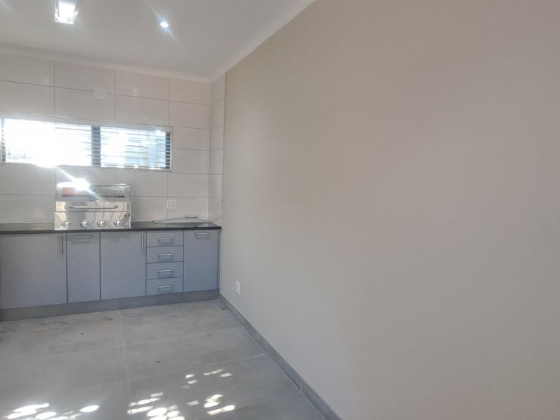 A clean, modern kitchen area featuring grey built-in cabinetry, a stainless steel sink, tiled splashbacks, and a built-in gas braai unit.