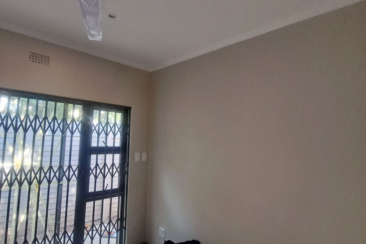 A vacant bedroom featuring neutral walls, a ceiling fan, and a sliding door with a security gate leading to the exterior.