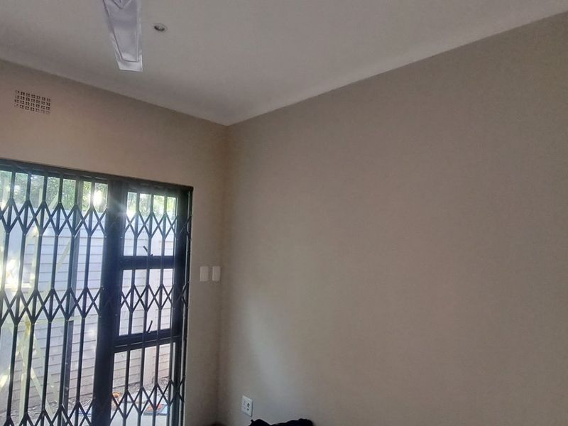 A vacant bedroom featuring neutral walls, a ceiling fan, and a sliding door with a security gate leading to the exterior.