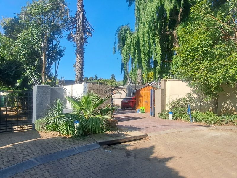 Front exterior view featuring a paved driveway, secure metal gate, perimeter wall with electric fencing, and established garden landscaping.