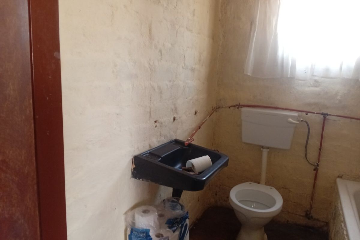 A small, dated bathroom featuring a wall-mounted basin, toilet, and bathtub with exposed plumbing and unfinished wall surfaces requiring renovation.