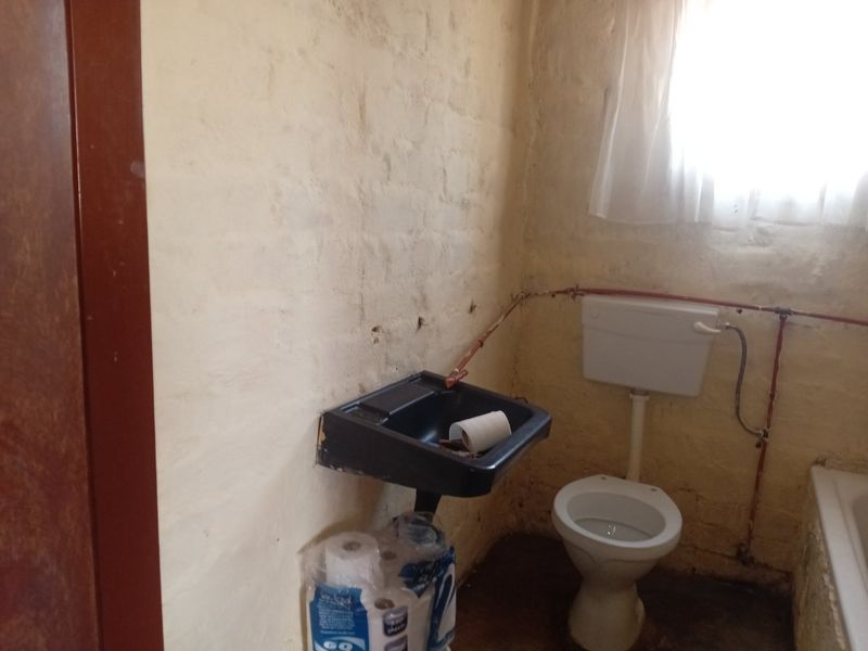 A small, dated bathroom featuring a wall-mounted basin, toilet, and bathtub with exposed plumbing and unfinished wall surfaces requiring renovation.