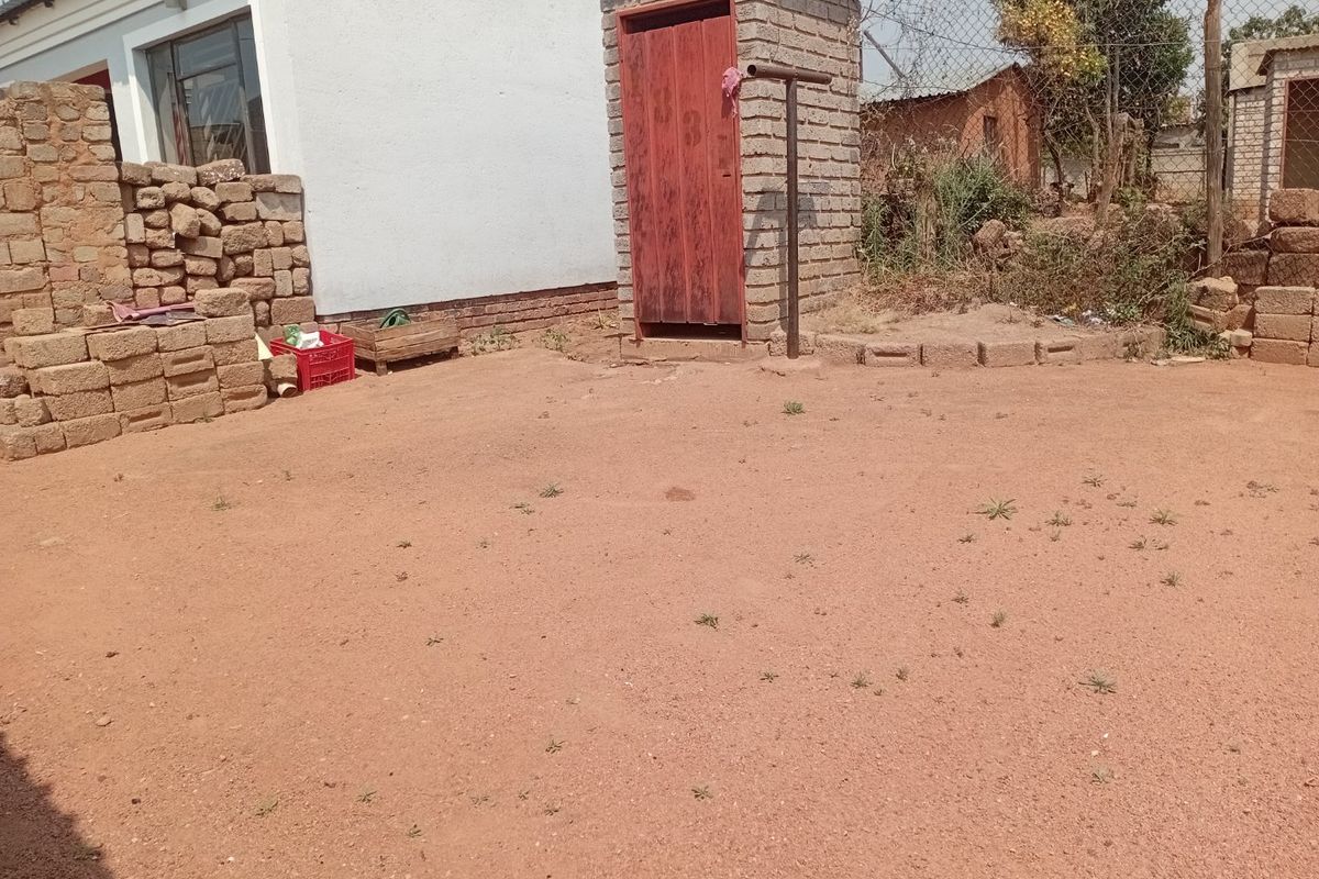 Rear exterior area featuring a small brick outbuilding, chain link fencing, and an unpaved yard space.