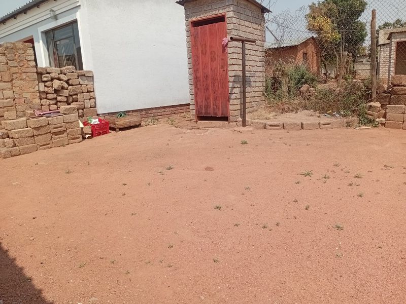 Rear exterior area featuring a small brick outbuilding, chain link fencing, and an unpaved yard space.