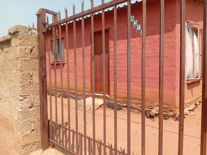 Front exterior view of a townhouse featuring a metal security gate, spiked fencing, and a plastered facade with visible signs of wear.