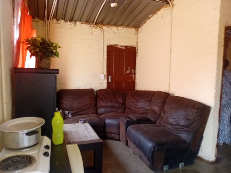 An open-plan living area featuring exposed brick walls, a corrugated metal ceiling, and exposed electrical conduit, requiring significant cosmetic renovation.