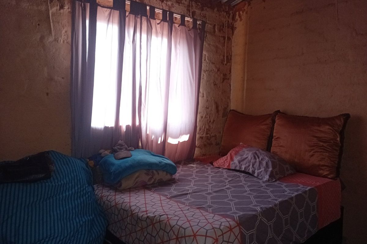 A bedroom featuring exposed brick walls and a corrugated metal ceiling, requiring significant renovation and finishing to improve the living space.