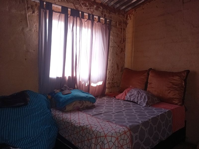A bedroom featuring exposed brick walls and a corrugated metal ceiling, requiring significant renovation and finishing to improve the living space.