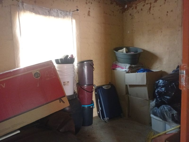 A small utility or storage room featuring a window and showing significant signs of wall surface deterioration and peeling paint.