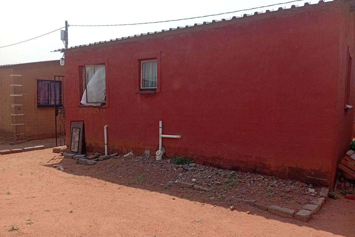 Rear exterior view of a townhouse featuring a red painted facade, corrugated metal roofing, and exposed exterior plumbing infrastructure.