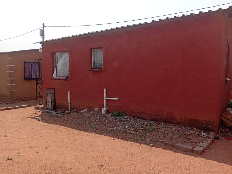 Rear exterior view of a townhouse featuring a red painted facade, corrugated metal roofing, and exposed exterior plumbing infrastructure.