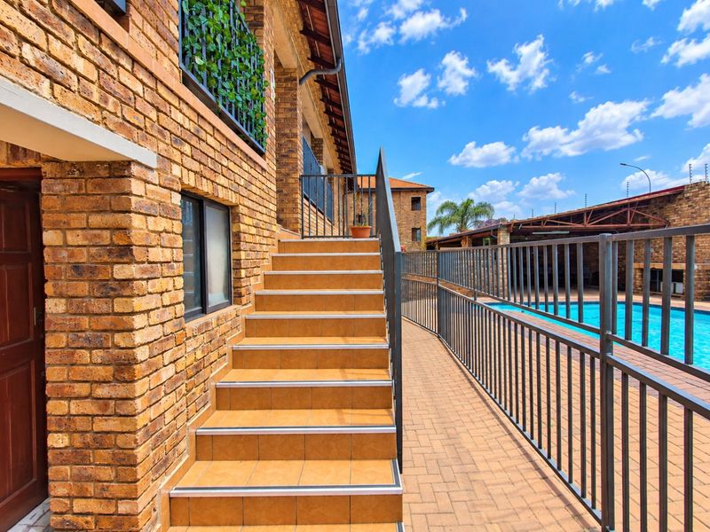 Exterior view of a face brick apartment building featuring a tiled staircase leading to a paved pool area with metal security fencing.