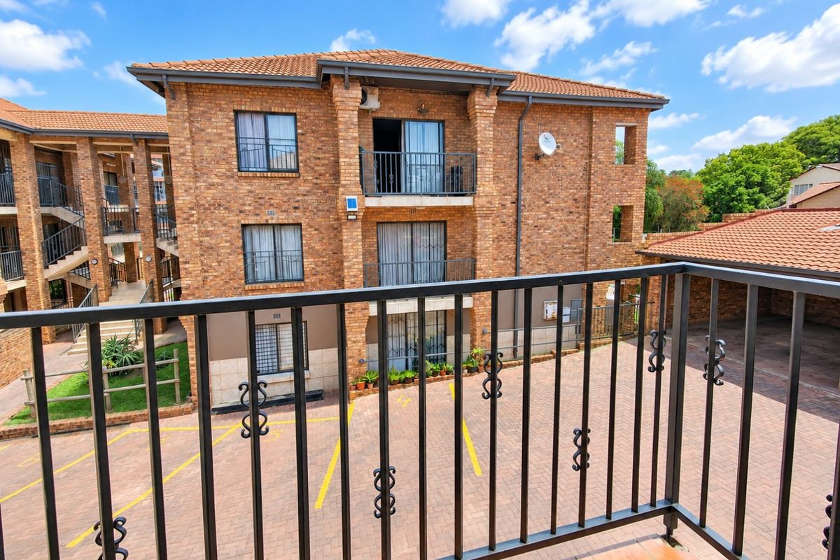 View of the apartment complex exterior featuring face brick construction, tiled roofing, and paved parking area with balcony access.