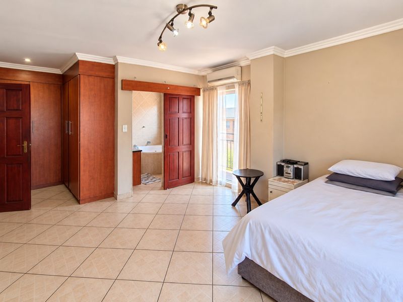 Spacious bedroom featuring tiled flooring, built-in wooden cupboards, an en-suite bathroom, and an air conditioning unit with access to a small balcony.