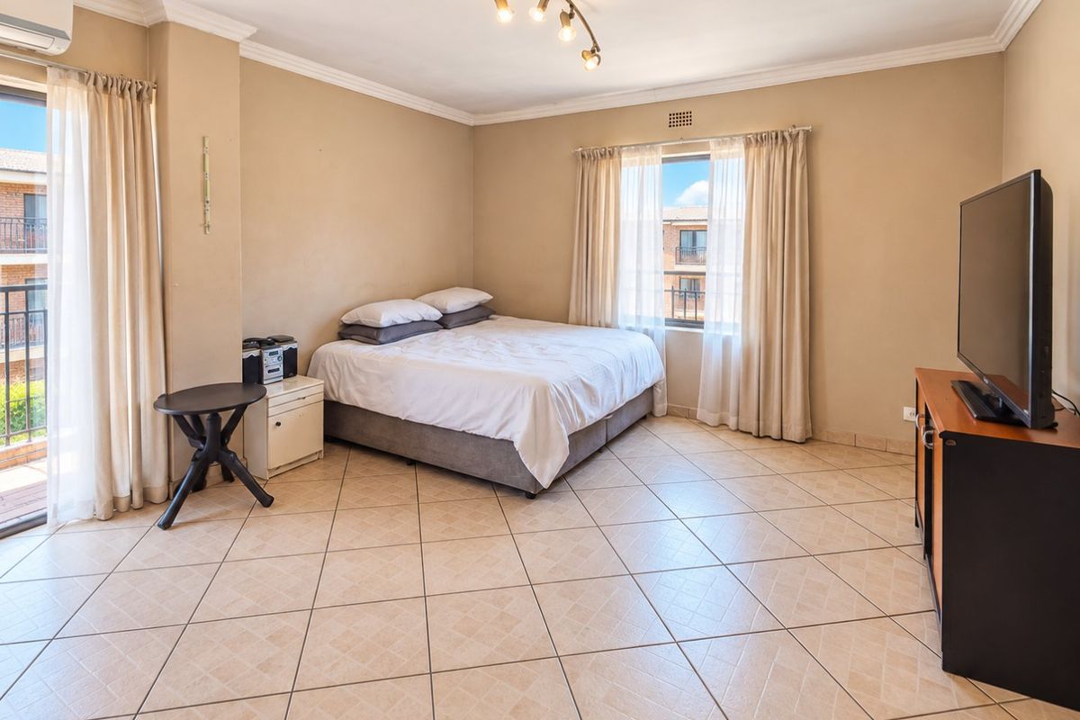 Spacious bedroom featuring ceramic tiled flooring, an air conditioning unit, and direct access to a private balcony through a sliding glass door.