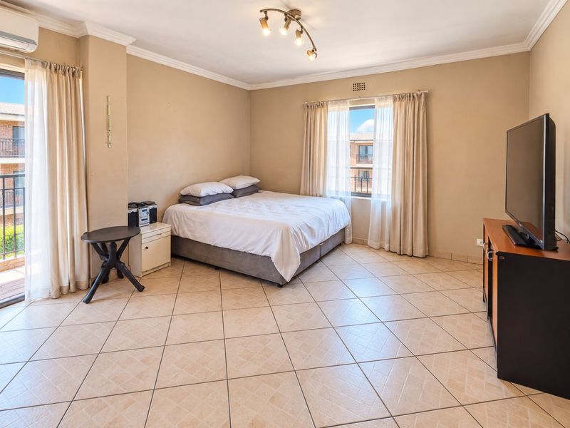 Spacious bedroom featuring ceramic tiled flooring, an air conditioning unit, and direct access to a private balcony through a sliding glass door.