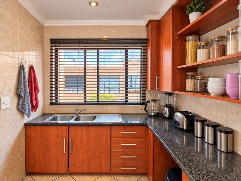 A well-maintained kitchen featuring wooden cabinetry, granite countertops, a double basin stainless steel sink, and tiled wall finishes.