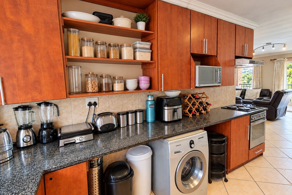 A functional kitchen featuring warm-toned wooden cabinetry, granite countertops, built-in appliances, and tiled flooring, seamlessly flowing into the adjacent living area.