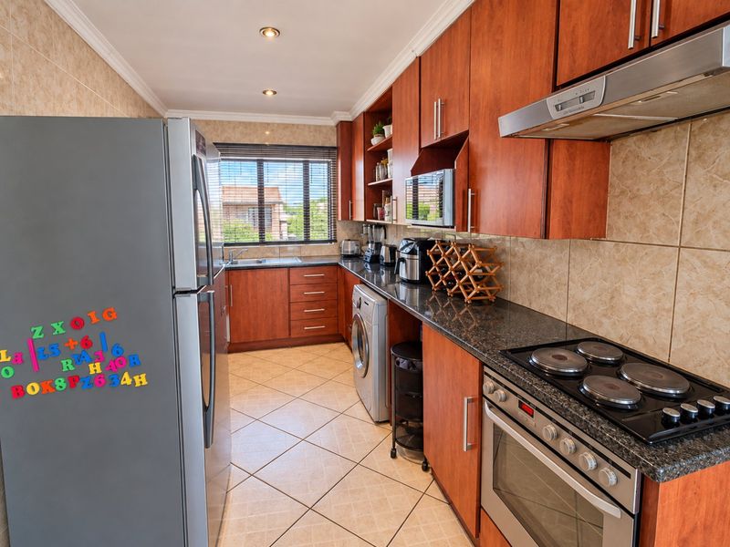 A functional kitchen featuring warm-toned wooden cabinetry, granite countertops, a built-in oven with electric hob, and tiled finishes throughout.