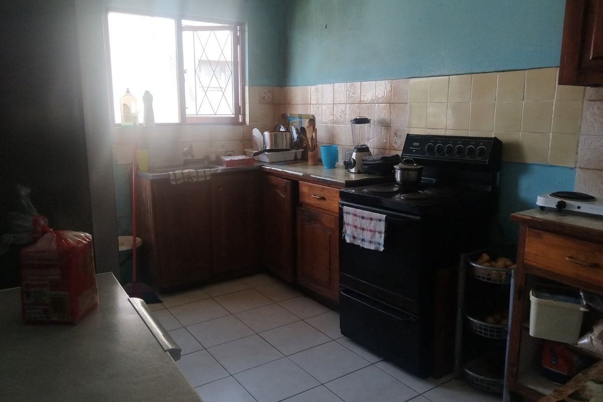A functional kitchen featuring wooden cabinetry, tiled backsplash, and ceramic flooring, offering a dated aesthetic with potential for modernization.