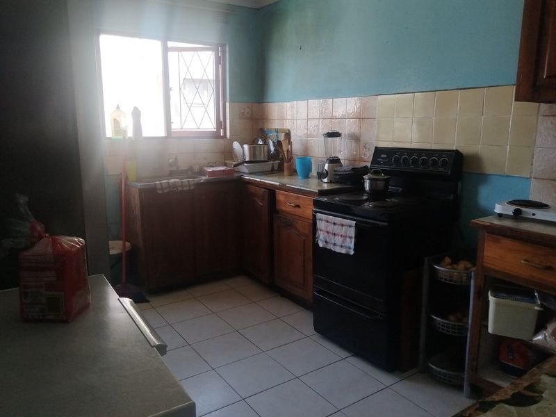 A functional kitchen featuring wooden cabinetry, tiled backsplash, and ceramic flooring, offering a dated aesthetic with potential for modernization.