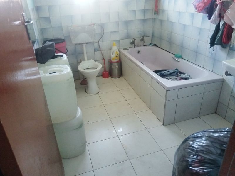A dated bathroom featuring a bathtub and toilet with tiled finishes, requiring renovation to modernize the space and improve overall condition.