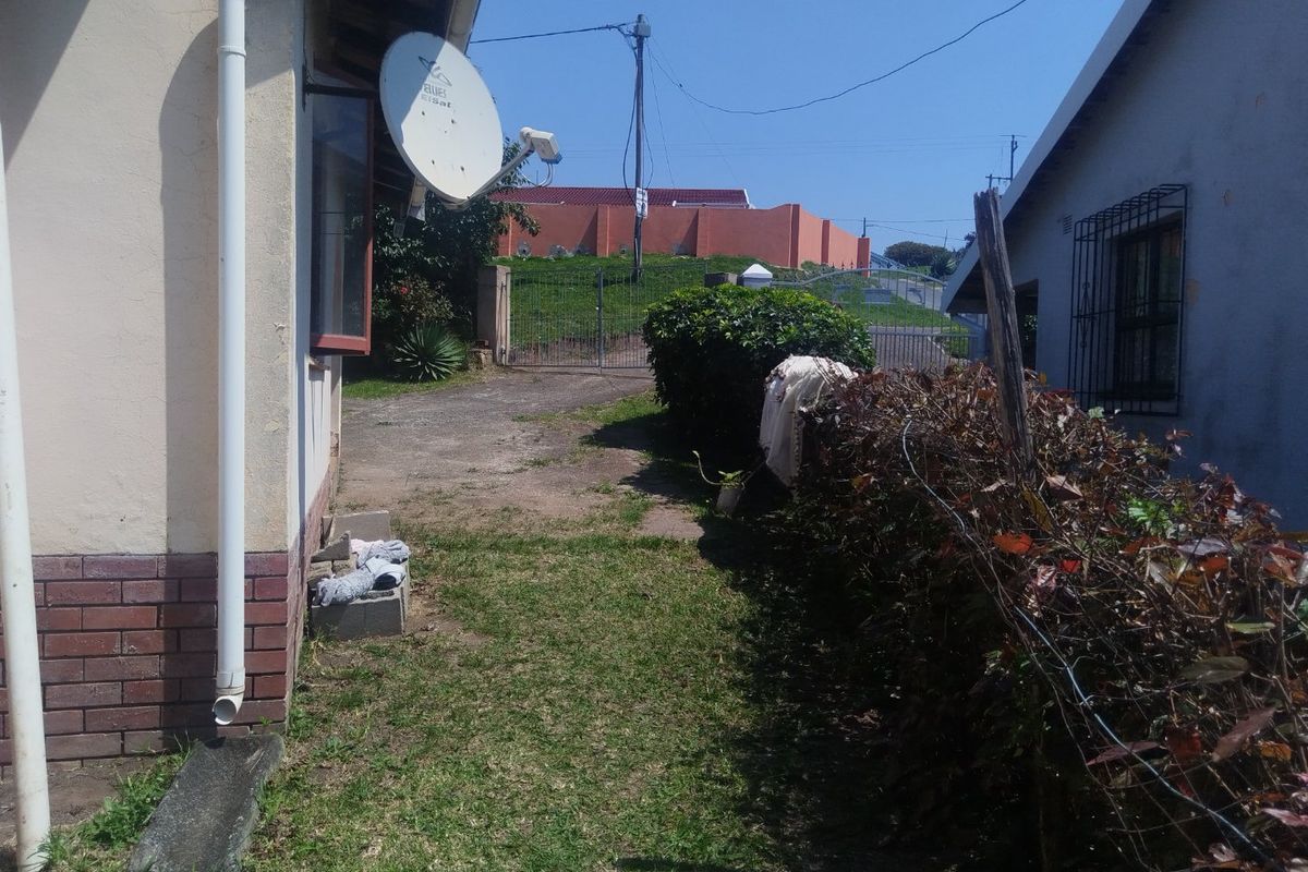 A view of the side and rear exterior area featuring a lawn, boundary hedge, and basic building infrastructure including a satellite dish and security bars.