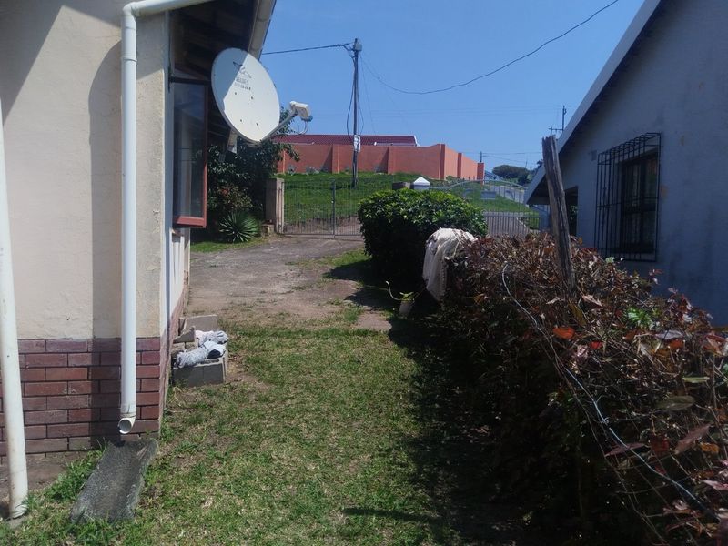 A view of the side and rear exterior area featuring a lawn, boundary hedge, and basic building infrastructure including a satellite dish and security bars.