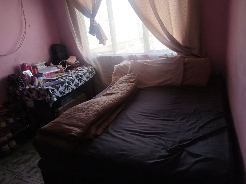 A compact bedroom featuring tiled flooring and a large window, providing natural light to the space.