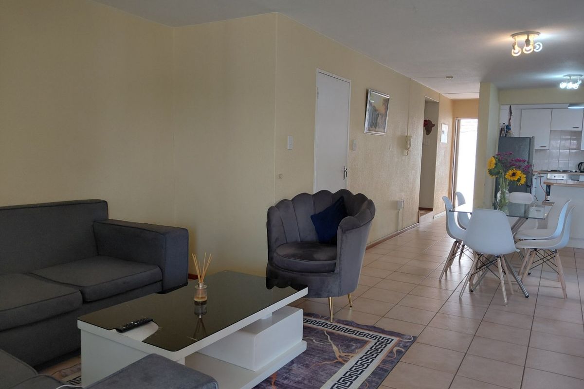 Open-plan living and dining area featuring tiled flooring and a functional kitchen with built-in cabinetry and appliances.