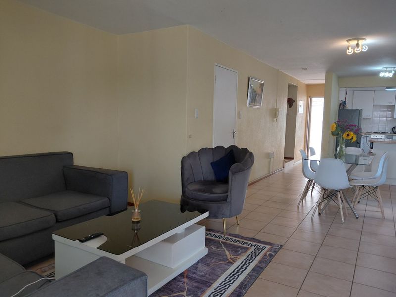 Open-plan living and dining area featuring tiled flooring and a functional kitchen with built-in cabinetry and appliances.