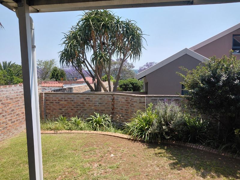 A view from a covered patio overlooking a private garden with established trees and a brick boundary wall.