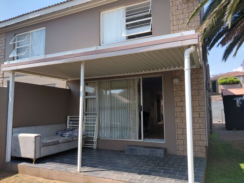 A covered patio area featuring tiled flooring, stone cladding accents, and a sliding glass door providing access to the interior of the townhouse.