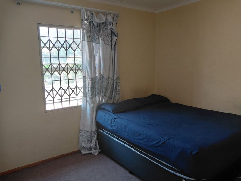 A simple bedroom featuring carpeted flooring and a window fitted with a security gate.